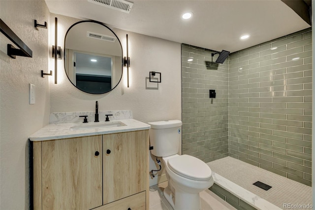 bathroom with toilet, visible vents, a tile shower, and vanity