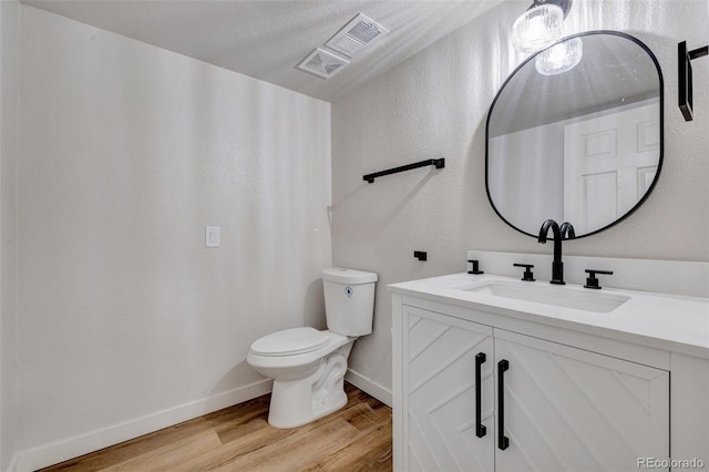 half bath with vanity, toilet, baseboards, wood finished floors, and visible vents