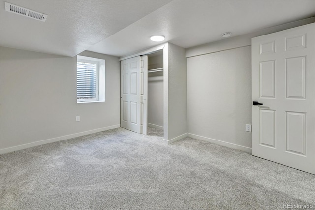 unfurnished bedroom featuring carpet flooring, a textured ceiling, baseboards, visible vents, and a closet