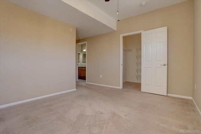 unfurnished bedroom featuring a walk in closet, light carpet, connected bathroom, and a closet