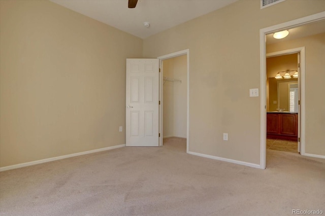 unfurnished bedroom with a closet, ceiling fan, light carpet, a spacious closet, and baseboards