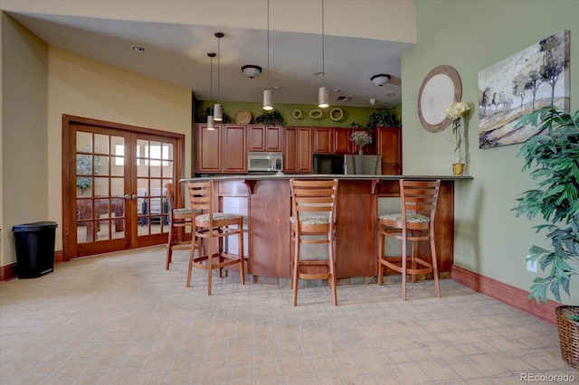 kitchen featuring hanging light fixtures, french doors, a breakfast bar, brown cabinetry, and stainless steel microwave