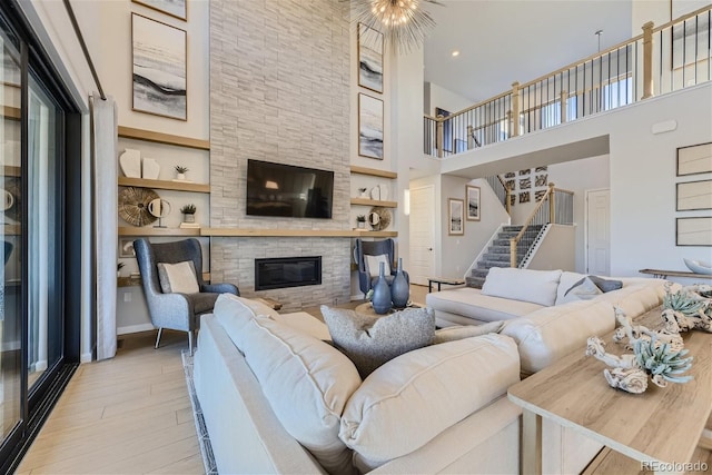 living room with a high ceiling, light hardwood / wood-style flooring, a stone fireplace, and built in shelves