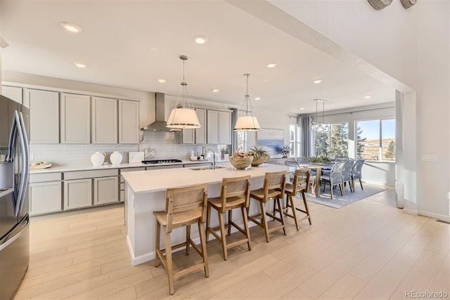 kitchen featuring wall chimney exhaust hood, decorative light fixtures, a center island with sink, and gray cabinetry