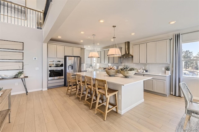 kitchen featuring a center island, hanging light fixtures, stainless steel appliances, wall chimney exhaust hood, and light hardwood / wood-style flooring