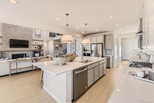 kitchen featuring appliances with stainless steel finishes, sink, hanging light fixtures, gray cabinets, and a center island with sink