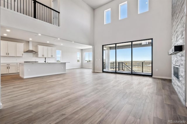 unfurnished living room featuring recessed lighting, baseboards, a stone fireplace, and light wood finished floors