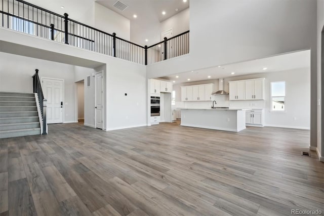 unfurnished living room with light wood-style floors, visible vents, a sink, and stairs