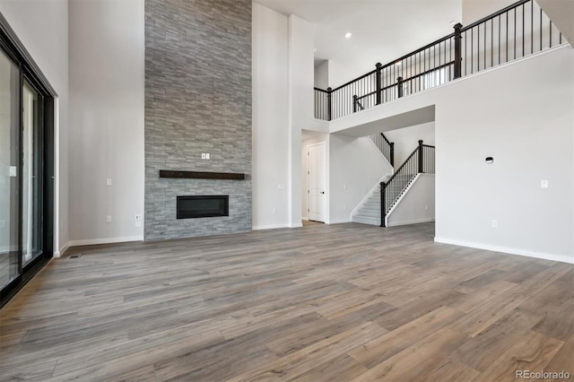 unfurnished living room featuring stairway, a high ceiling, a stone fireplace, wood finished floors, and baseboards