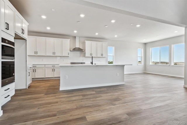 kitchen with recessed lighting, white cabinets, wall chimney range hood, and light wood finished floors