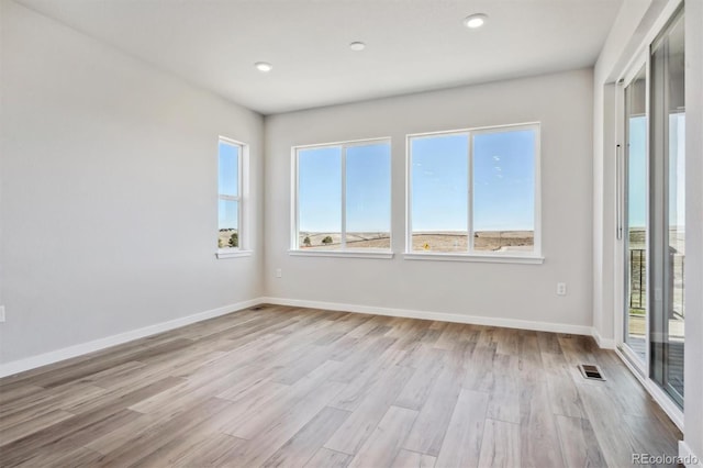 spare room featuring visible vents, light wood-style floors, a wealth of natural light, and baseboards