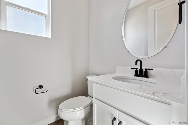 half bathroom featuring toilet, vanity, and baseboards