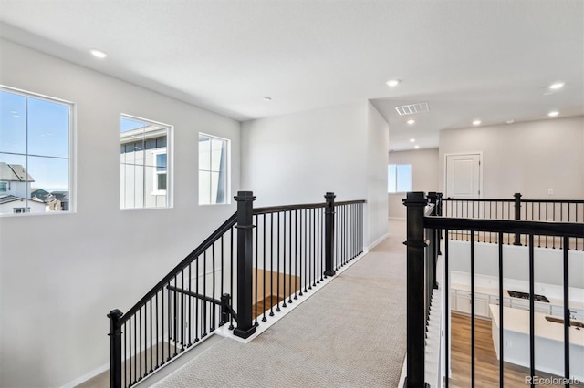 hallway featuring recessed lighting, plenty of natural light, visible vents, and an upstairs landing