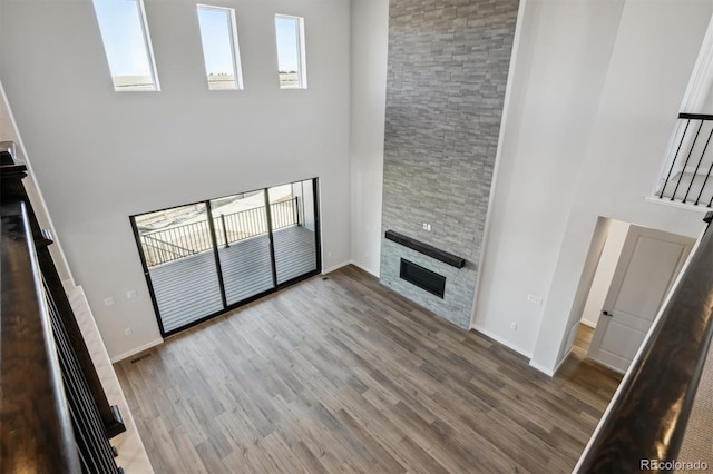 unfurnished living room with a fireplace, a towering ceiling, baseboards, and wood finished floors