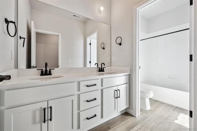 bathroom featuring toilet, double vanity, a sink, and visible vents