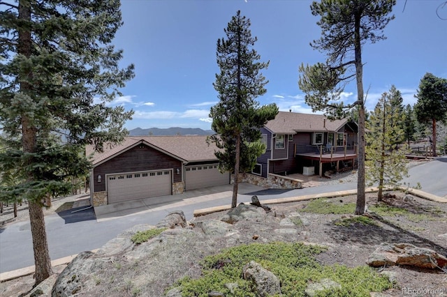 32091 Black Widow Dr, Conifer, CO 80433 - view of front of home with stone siding, a wooden deck, a garage, and driveway