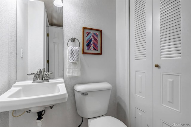 bathroom with toilet, a closet, a sink, and a textured wall