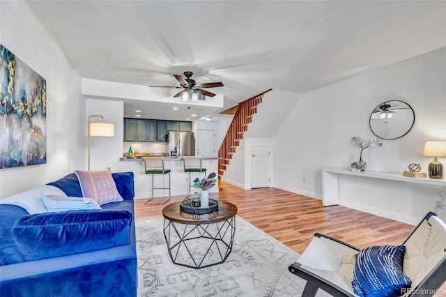 living area featuring baseboards, stairway, a ceiling fan, and light wood-style floors