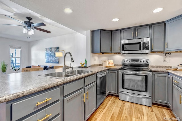 kitchen featuring light wood finished floors, stainless steel appliances, gray cabinetry, a sink, and recessed lighting