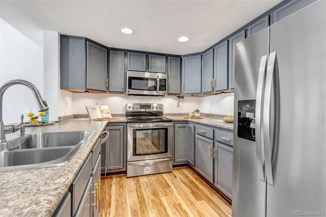 kitchen featuring a textured ceiling, light wood-style flooring, recessed lighting, stainless steel appliances, and a sink