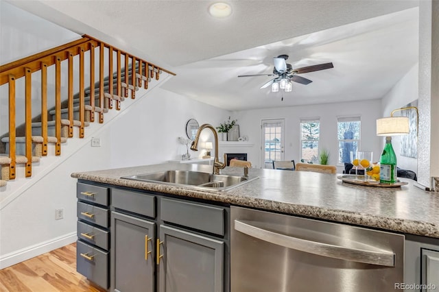 kitchen with light wood-style flooring, a fireplace, a sink, stainless steel dishwasher, and gray cabinets