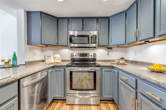 kitchen featuring light wood finished floors, appliances with stainless steel finishes, a textured ceiling, and blue cabinetry