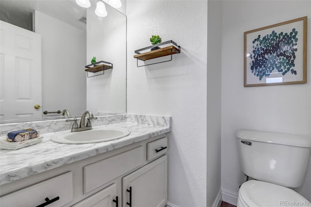 half bath featuring baseboards, visible vents, vanity, and toilet