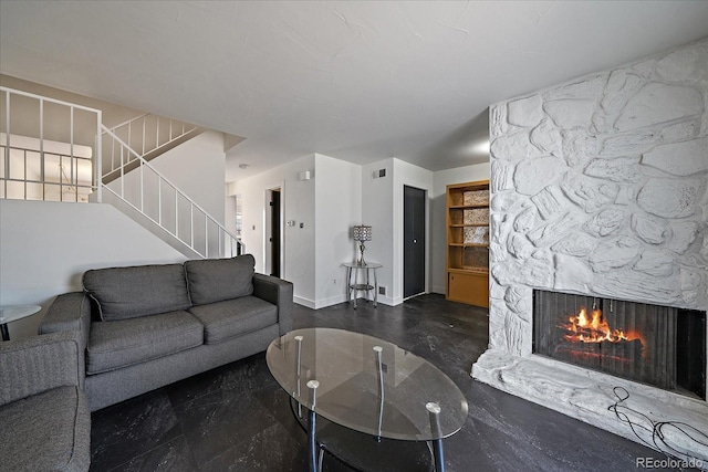 living room featuring stairway, baseboards, a stone fireplace, and visible vents