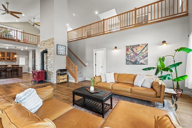 living area with a wood stove, stairs, a ceiling fan, and wood finished floors