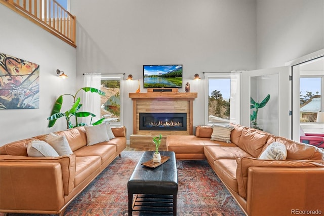 living room featuring a glass covered fireplace, a healthy amount of sunlight, and a high ceiling