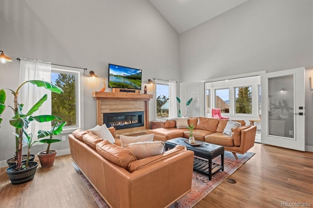 living area featuring baseboards, high vaulted ceiling, wood finished floors, and a glass covered fireplace