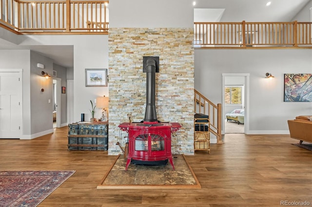 living room featuring a towering ceiling, wood finished floors, a wood stove, and baseboards