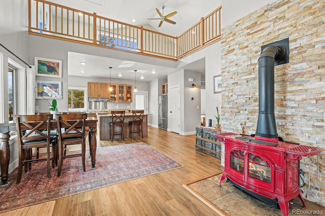 living area featuring a towering ceiling, a wood stove, ceiling fan, light wood-type flooring, and baseboards