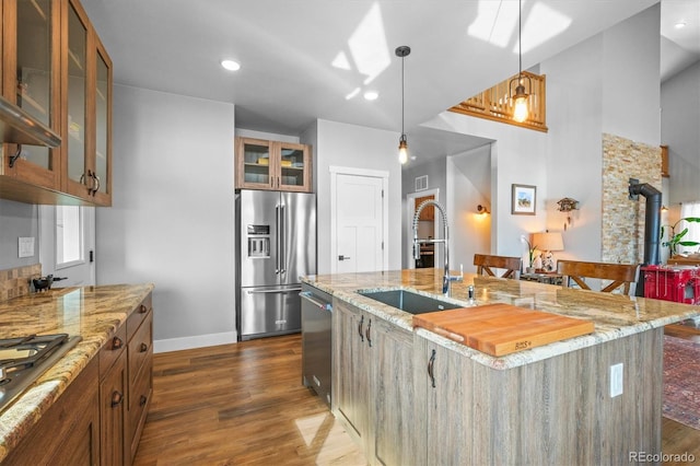 kitchen featuring a center island with sink, dark wood-style floors, glass insert cabinets, stainless steel appliances, and a sink