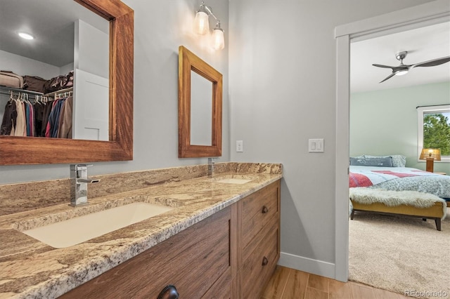 ensuite bathroom with double vanity, ceiling fan, a sink, and wood finished floors