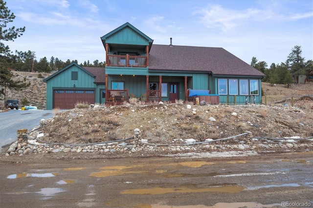 rustic home with aphalt driveway, roof with shingles, covered porch, a balcony, and a garage