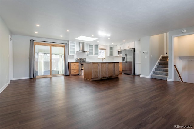 kitchen with white cabinetry, appliances with stainless steel finishes, a kitchen island, a healthy amount of sunlight, and wall chimney range hood