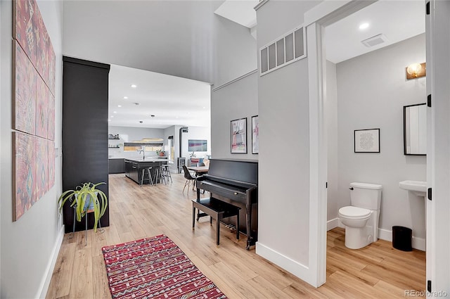 hallway with light wood finished floors, visible vents, and baseboards