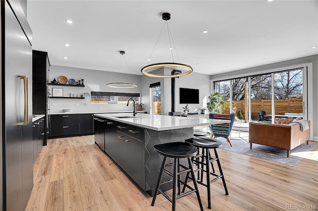 kitchen featuring light countertops, light wood-style floors, a sink, stainless steel built in refrigerator, and dark cabinetry