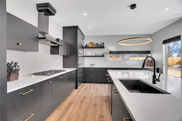 kitchen featuring stainless steel appliances, a sink, light countertops, light wood-type flooring, and wall chimney exhaust hood