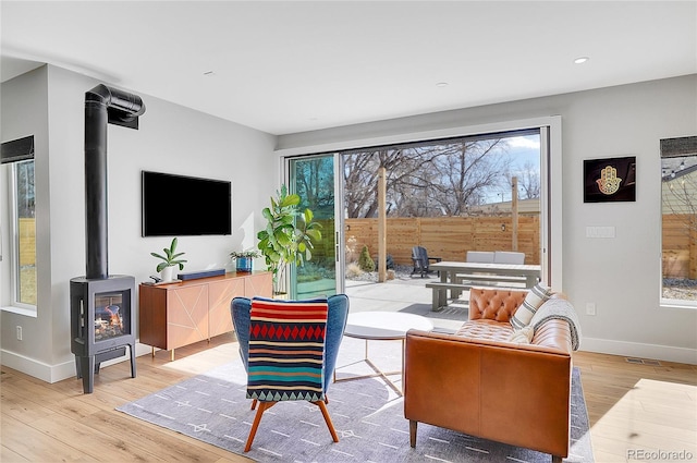 living area with recessed lighting, wood finished floors, visible vents, baseboards, and a wood stove