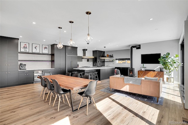 dining area with wine cooler, light wood-style flooring, a wood stove, and recessed lighting