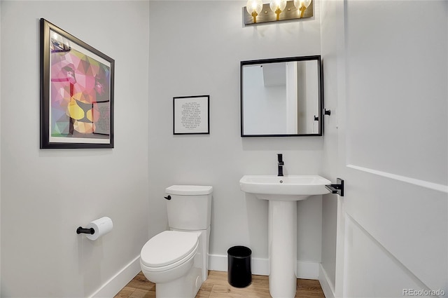 bathroom with toilet, a sink, baseboards, and wood finished floors