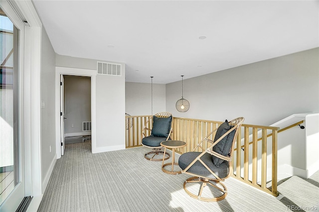 sitting room with carpet floors, baseboards, visible vents, and an upstairs landing