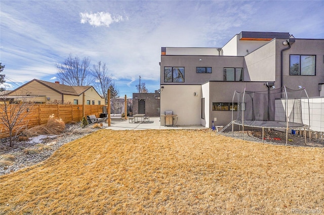 rear view of house featuring a patio, a fenced backyard, a lawn, stucco siding, and a trampoline