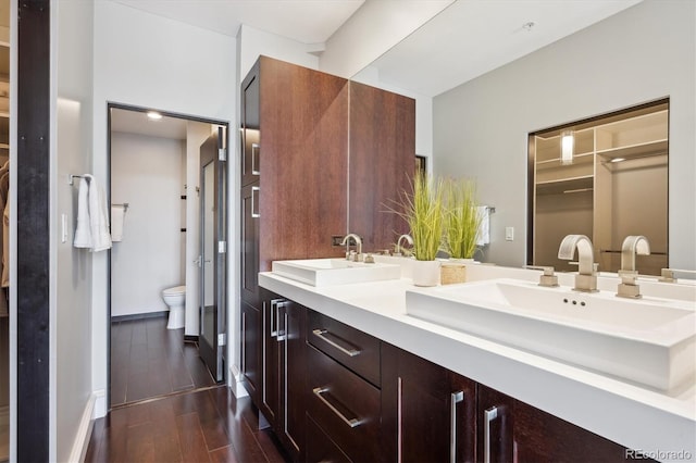 4875 S Monaco St Unit 303, Denver, CO 80237 - full bathroom featuring toilet, double vanity, wood finished floors, and baseboards