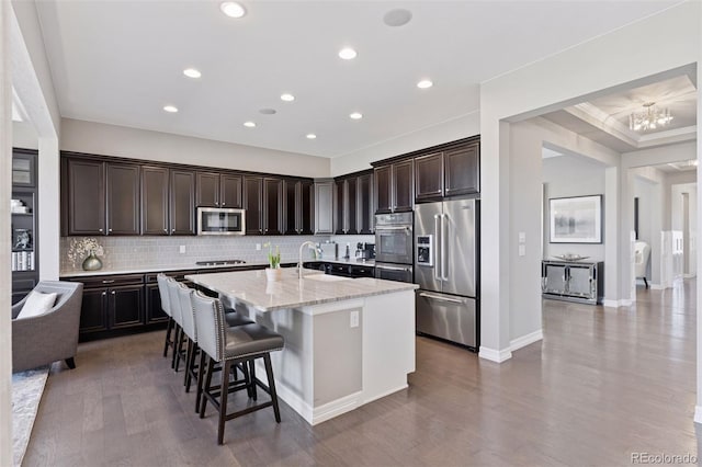 kitchen featuring a kitchen breakfast bar, appliances with stainless steel finishes, tasteful backsplash, a center island with sink, and dark brown cabinets