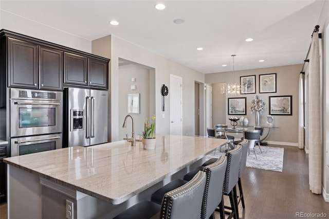 kitchen with a sink, dark wood finished floors, appliances with stainless steel finishes, and light stone countertops