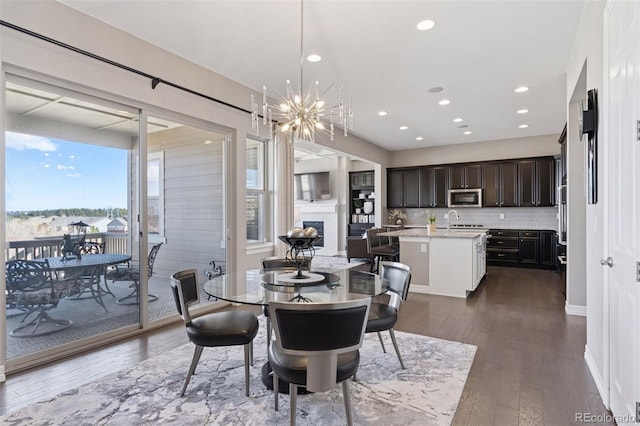dining space featuring dark wood-type flooring, recessed lighting, a chandelier, and a fireplace