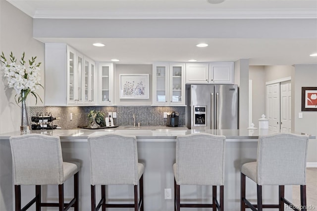 kitchen with stainless steel fridge, light countertops, decorative backsplash, and white cabinetry